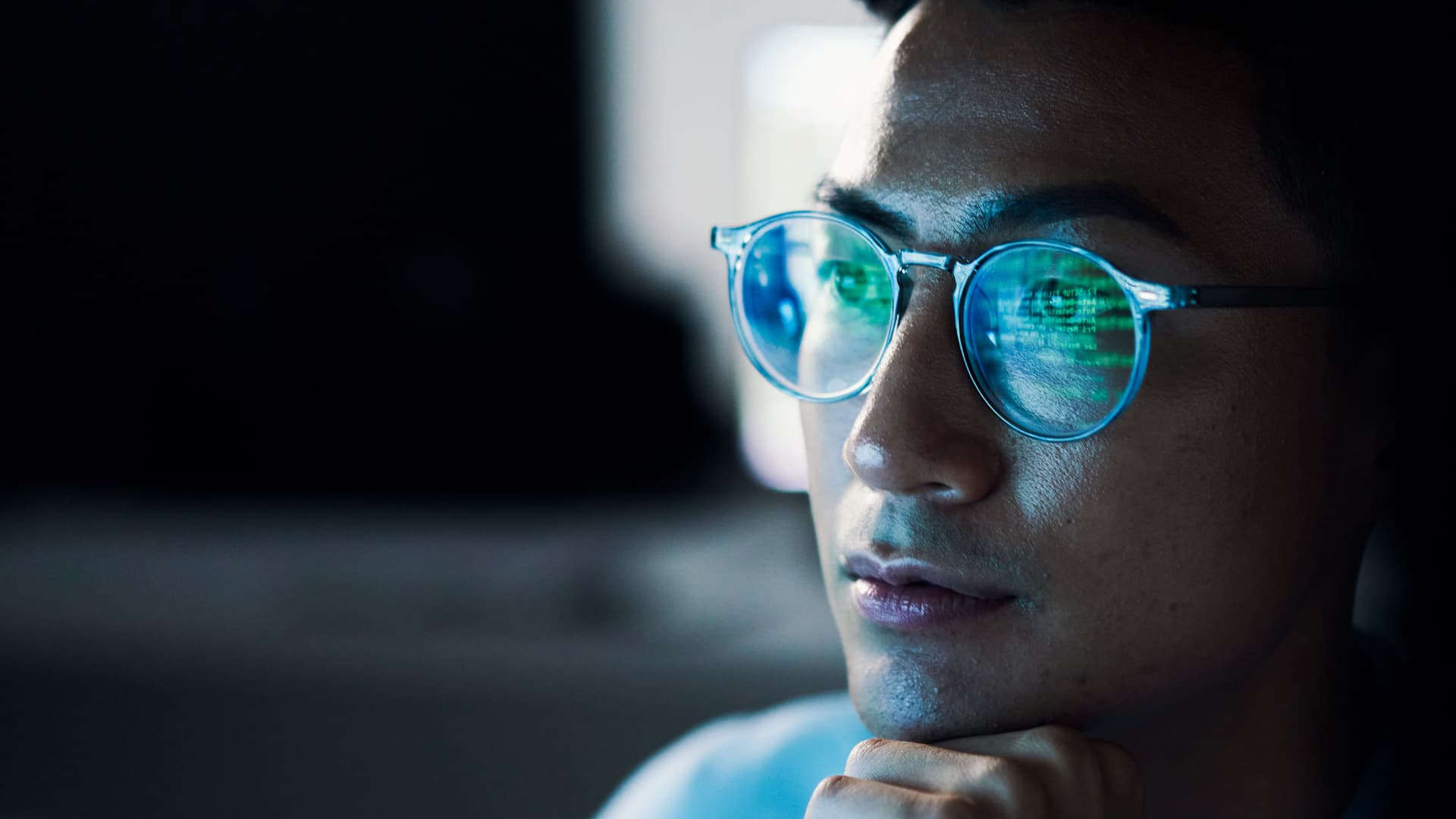 Asian man with computer code reflected in glasses.