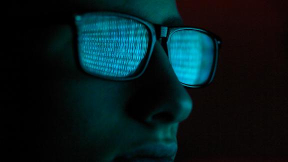 Cyber Crime, reflection in spectacles of virus hacking a computer, close up of face